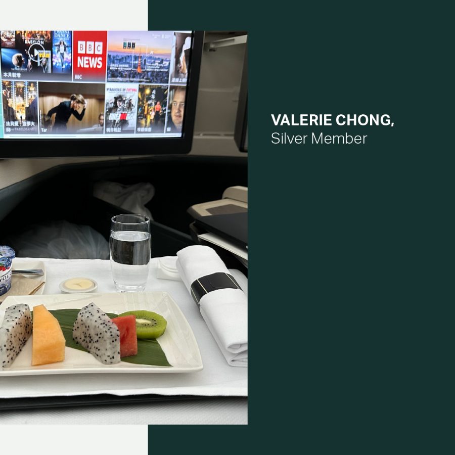 Fruit on a plate and a yoghurt pot with a screen above in the Business cabin on a Cathay Pacific flight.